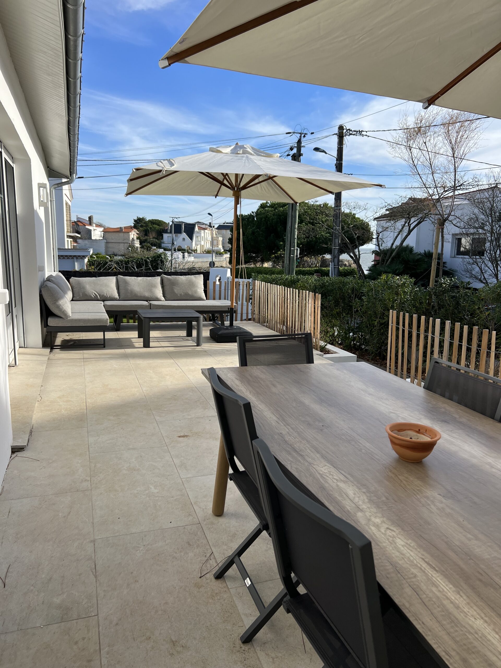 terrasse exposée au soleil de 30m2 avec salon bas, table pour 10 personnes, 2 parasols pour un peu d'ombre.